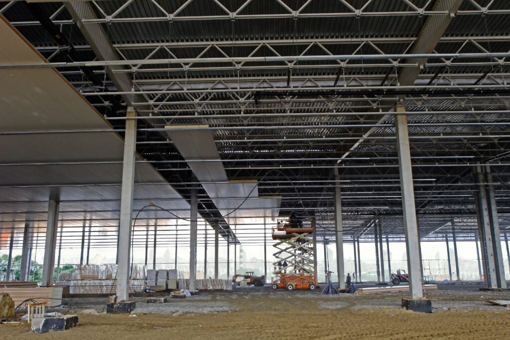 Workers use a scissor lift to install insulation panels on the ceiling of a new construction project in a commercial warehouse.